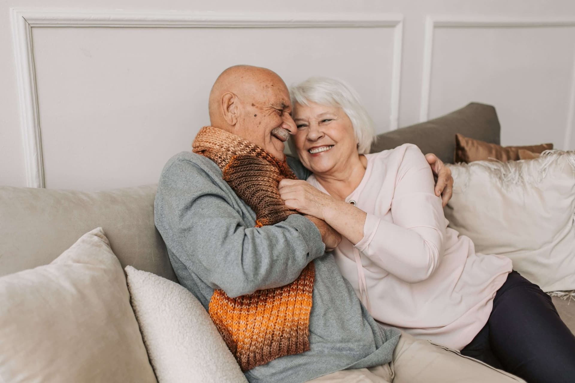 Älteres Paar sitzt lachend und umarmt auf einem Sofa im Wohnzimmer